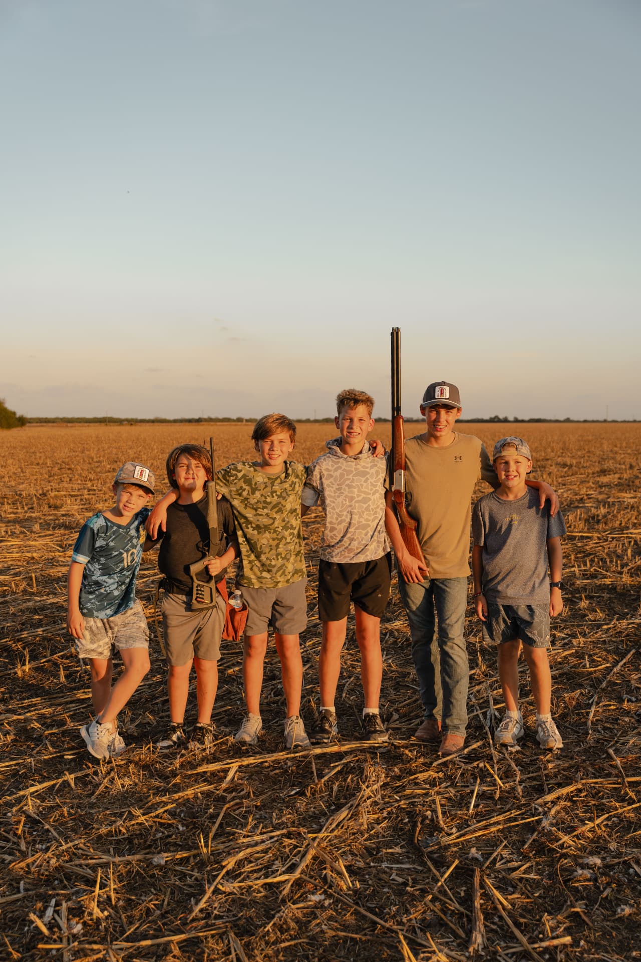 Six smiling boys posing in the field with their guns