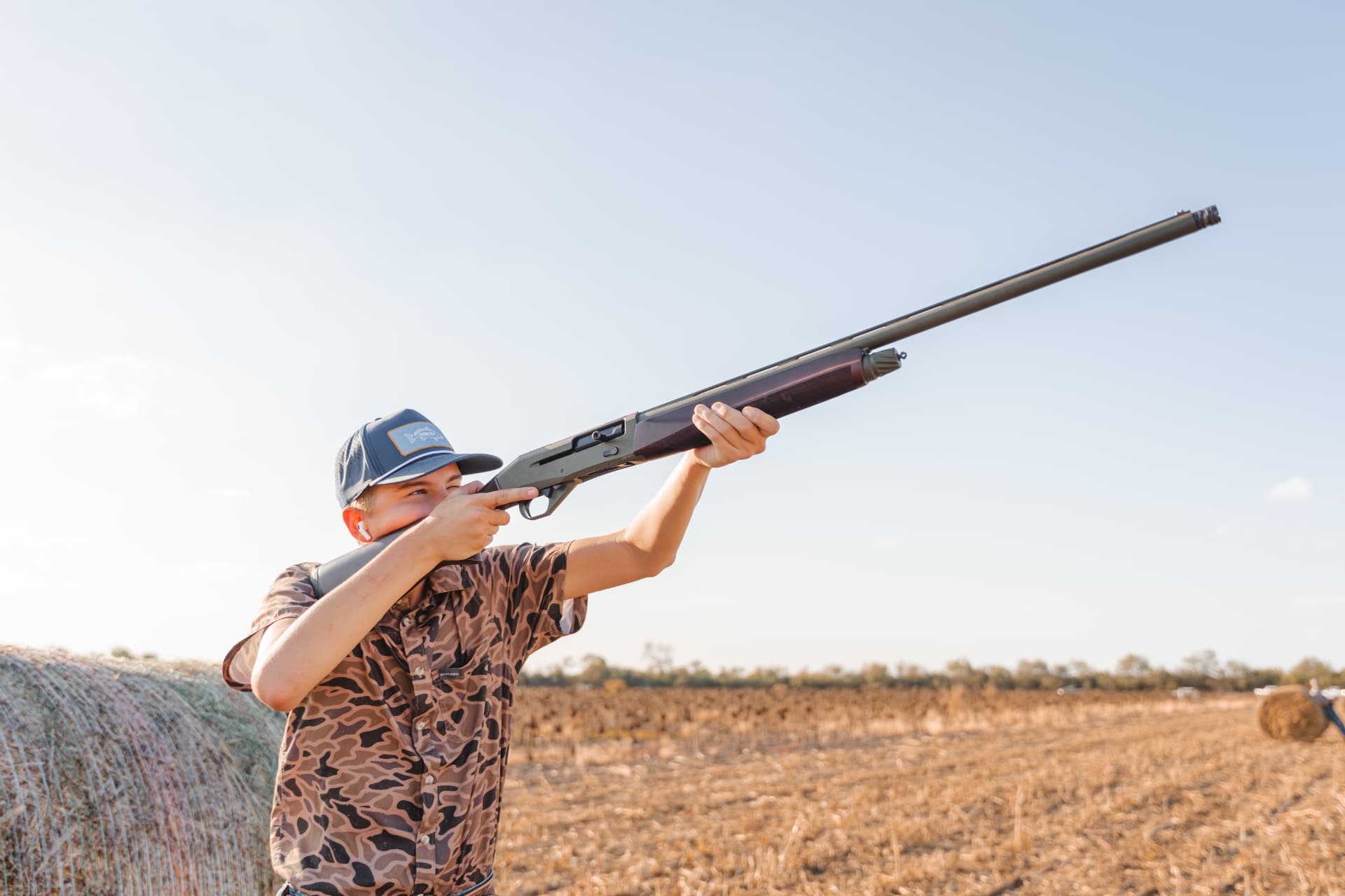 Young hunter taking aim from behind the round hay bale
