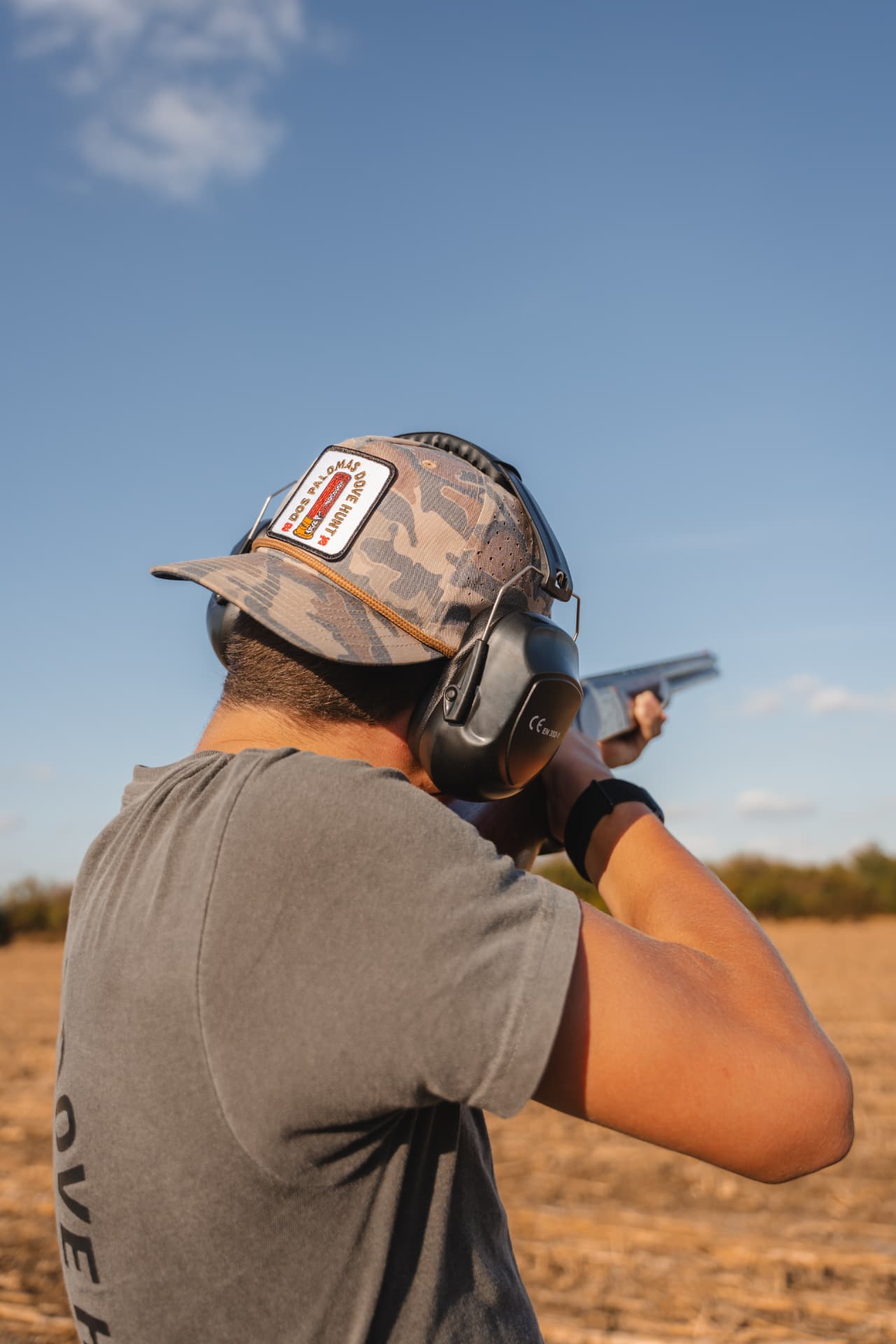 Hunter shouldering his shotgun under a wide blue sky