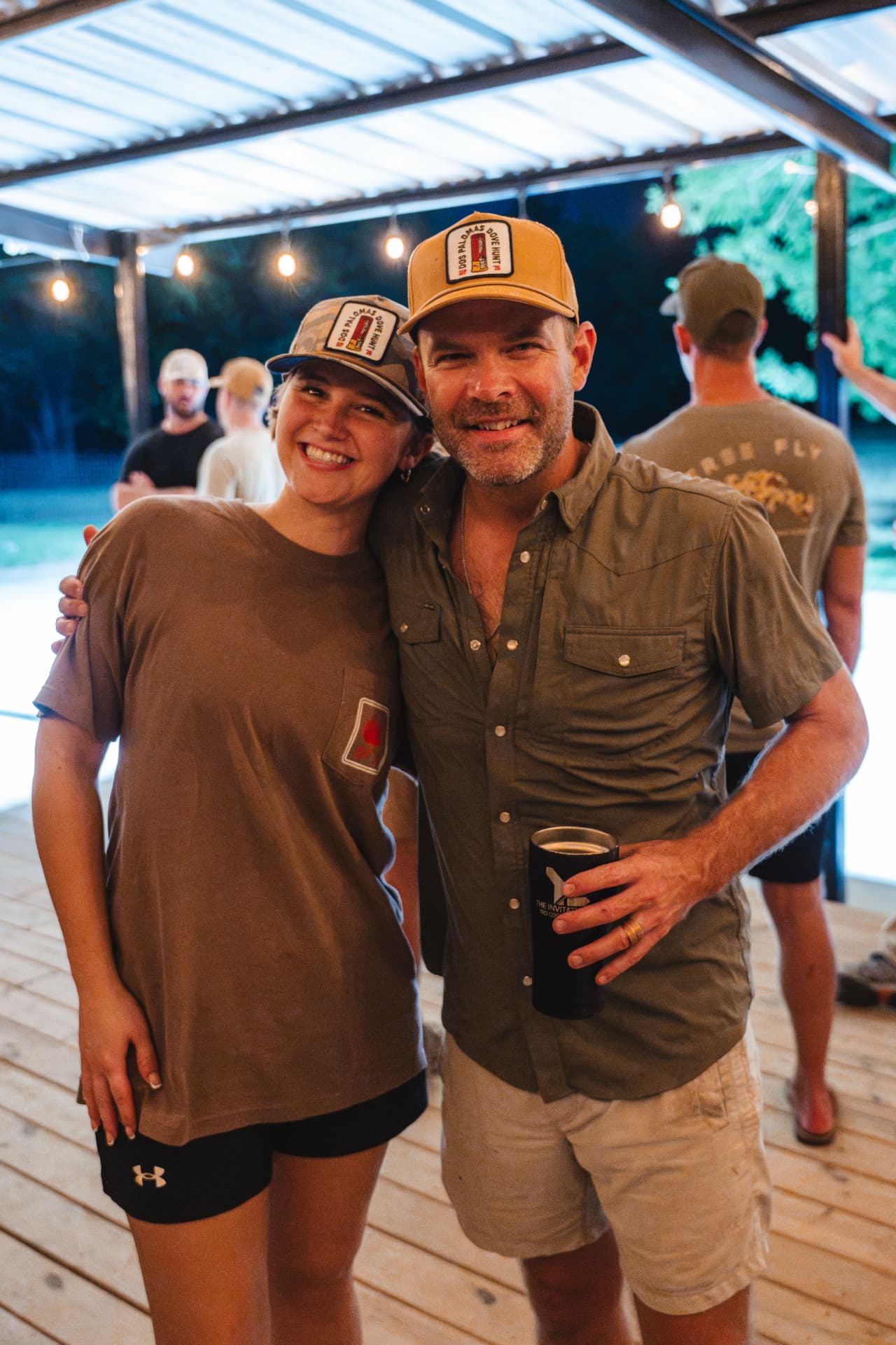 Smiling pair in hunt caps posing on the lit porch