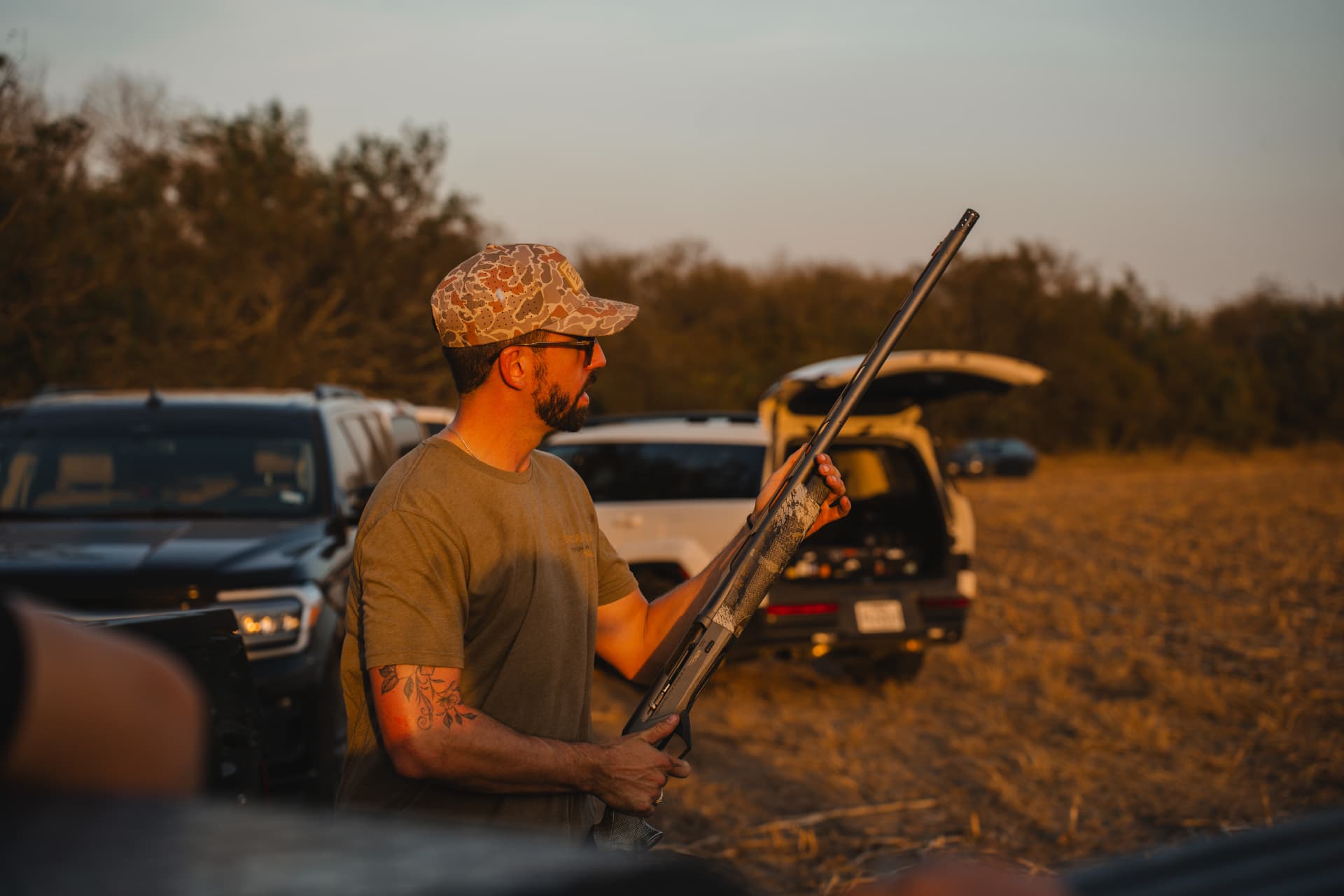 Hunter with his shotgun by the trucks at golden hour