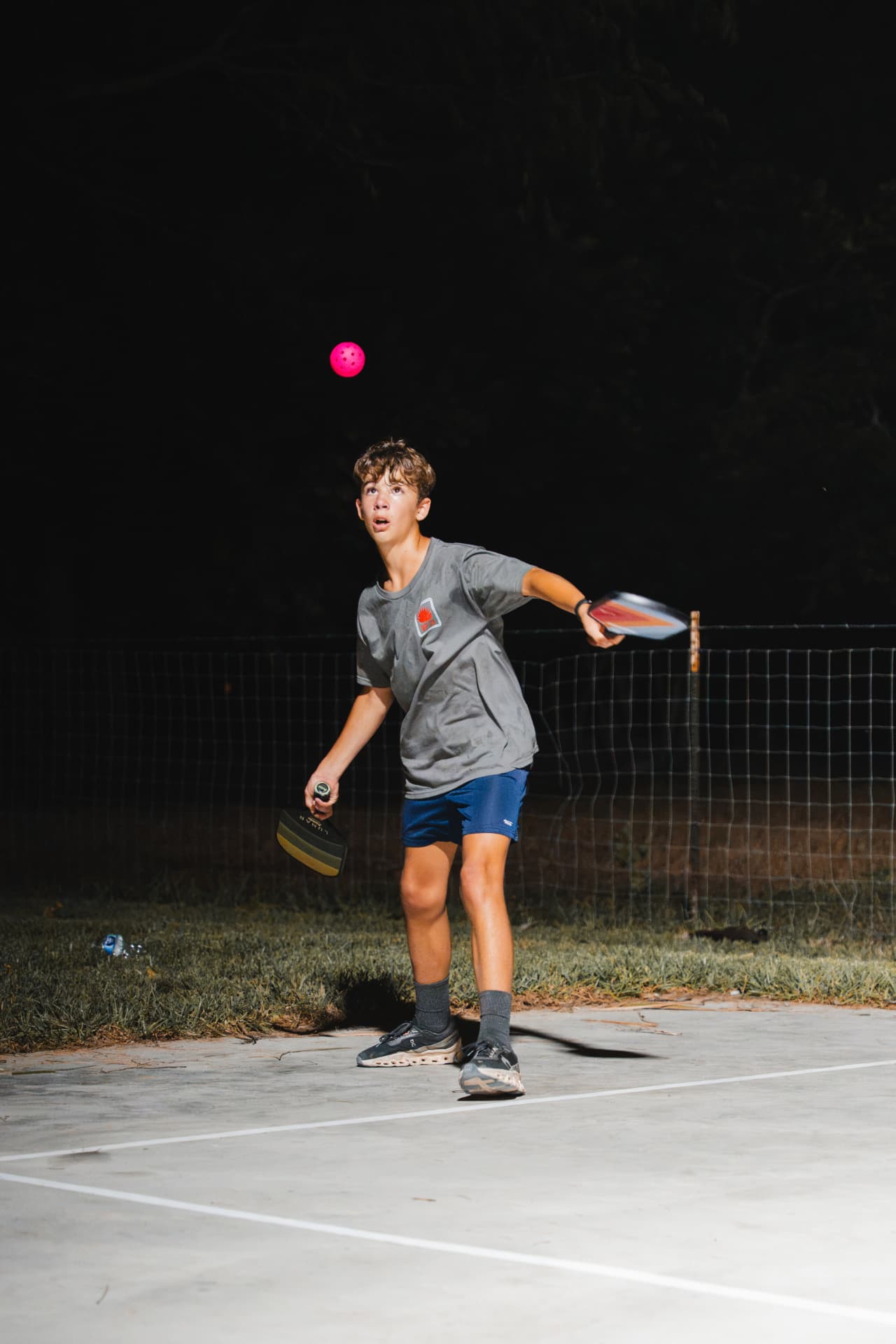 Young player tracking the ball with two paddles in hand