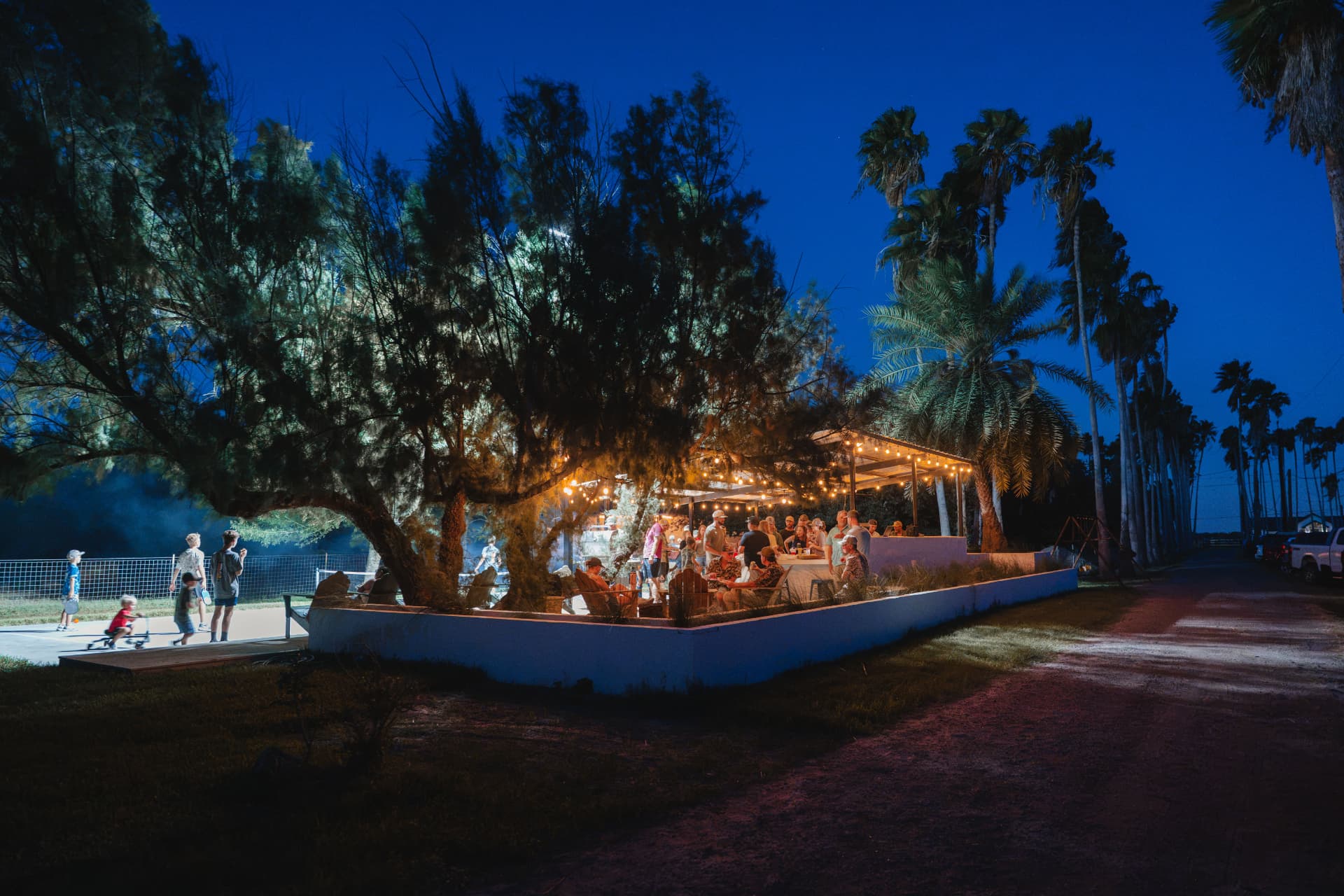 Guests gathering on the lit patio beside the trucks at night