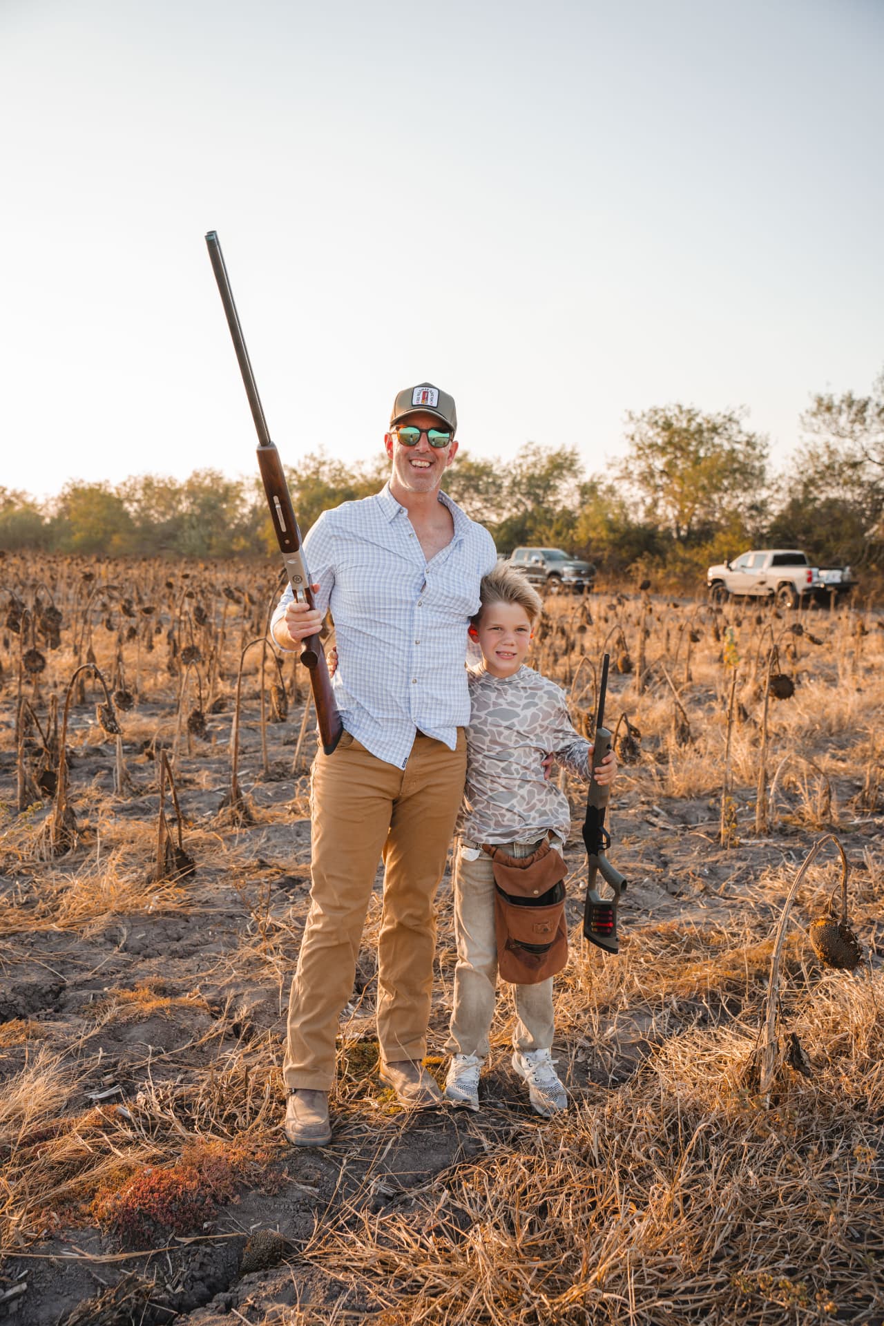 Father and son smiling with their shotguns in the sunflower field